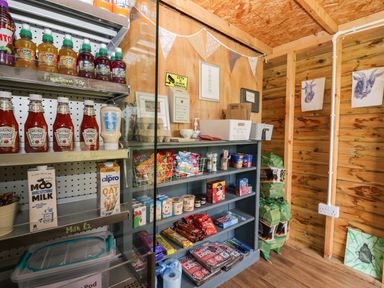 A small wooden shop interior with shelves stocked with ketchup, mayonnaise, drinks, snacks, and other grocery items at Orchard in Dalton-In-Furness