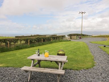 An outdoor area with a wooden picnic table with drinks a grassy lawn a gravel path and a fence at Orchard in Dalton-In-Furness