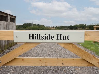 A wooden gate with a sign that reads Hillside Hut on a gravel path in a rural area at Hillside Hut in Radbourne near Ashbourne