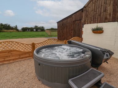 An outdoor hot tub with water bubbling next to a wooden fence and a wooden building at Hillside Hut in Radbourne near Ashbourne