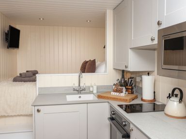 A compact kitchen with a sink stove kettle microwave and a small bed area with towels and pillows at Hillside Hut in Radbourne near Ashbourne