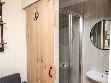 A bathroom with a glass shower enclosure, round mirror, and small sink next to a wooden door at Hillside Hut in Radbourne near Ashbourne