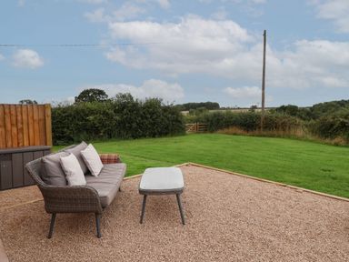 A garden patio with a sofa and table next to a lawn and wooden fence at Hillside Hut in Radbourne near Ashbourne