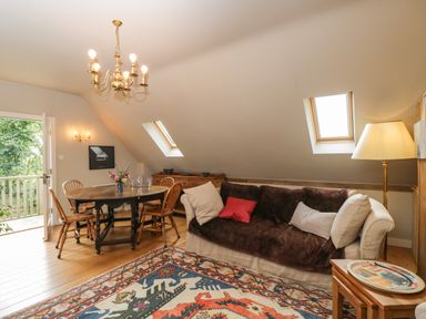 A living room with a sofa cushions a wooden dining table four chairs and a patterned rug at The Barn at Westhall Cottage Fulbrook near Burford