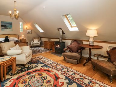 An attic bedroom with armchairs a bed a wood burning stove and skylight windows at The Barn at Westhall Cottage in Fulbrook near Burford