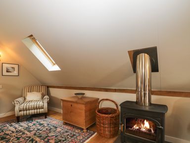 A room with a striped armchair wooden chest woven basket lit fireplace and skylight window at The Barn at Westhall Cottage Fulbrook near Burford