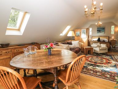 A room with a wooden dining table and chairs a sofa an armchair a bed and decorative rugs at The Barn at Westhall Cottage Fulbrook near Burford