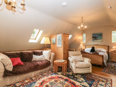 A room with a sofa and armchair near a wooden cabinet and bed with a stuffed toy at The Barn at Westhall Cottage Fulbrook near Burford