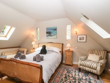 A bedroom with a double bed a striped armchair wooden side tables table lamps and skylights at The Barn at Westhall Cottage Fulbrook near Burford