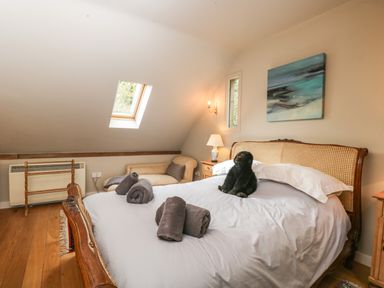 A bedroom with a wooden bed holding rolled towels and a stuffed animal with a chaise lounge and a skylight at The Barn at Westhall Cottage Fulbrook near Burford