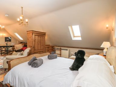 A bedroom with a bed with rolled towels and a stuffed gorilla a wooden wardrobe an armchair a dining table and skylights at The Barn at Westhall Cottage Fulbrook near Burford