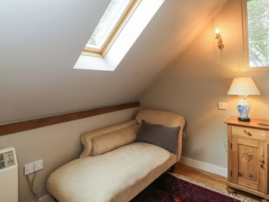 A beige chaise lounge with a dark cushion under a skylight with a wooden cabinet and table lamp nearby at The Barn at Westhall Cottage in Fulbrook near Burford