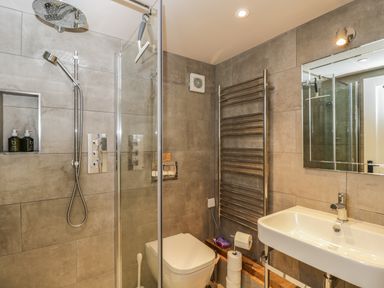 A bathroom with a shower area toilet sink mirror heated towel rack and toilet paper holder at The Barn at Westhall Cottage Fulbrook near Burford