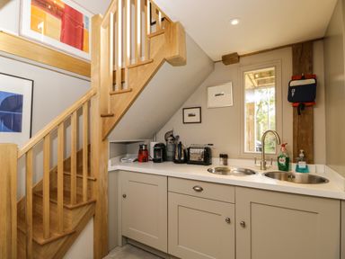 A kitchen area with a double sink and appliances under a wooden staircase at The Barn at Westhall Cottage Fulbrook near Burford