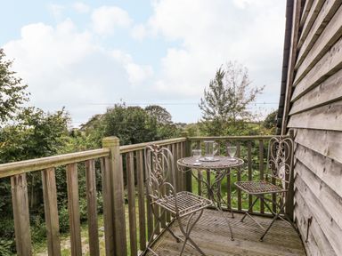 A wooden balcony with a metal table and two chairs overlooking trees at The Barn at Westhall Cottage in Fulbrook near Burford