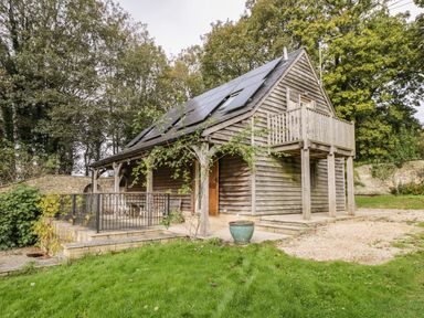 An outdoor view of a wooden house with solar panels on the roof a balcony on the upper floor a patio with furniture and a garden area at The Barn at Westhall Cottage Fulbrook near Burford