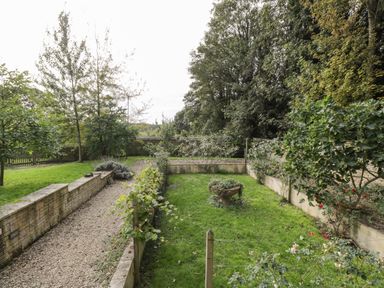 A garden with a gravel path bordered by stone walls and greenery at The Barn at Westhall Cottage Fulbrook near Burford