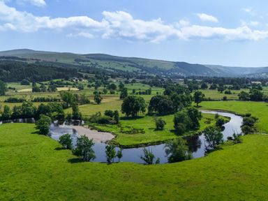 A river winding through a green landscape with trees and mountains at The Barn in Corwen