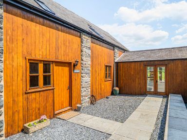 An outdoor view of a wooden structure with a stone wall and pathway at The Barn in Corwen