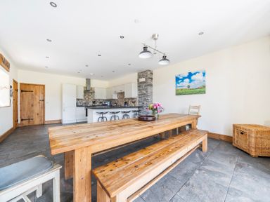 A dining room with a wooden table and kitchen area at The Barn in Corwen