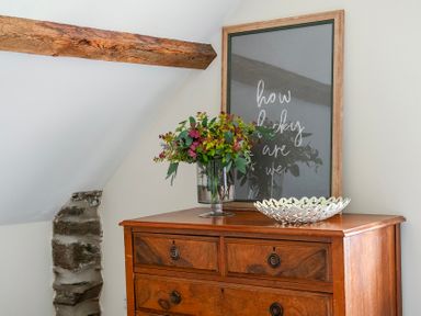 A bedroom with a dresser, flowers in a vase, and framed artwork at The Barn in Corwen