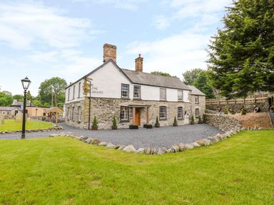 A stone and white exterior house with chimneys surrounded by grass and stone walls at The Druids in Druid near Corwen