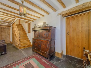 A hallway with wooden stairs wooden doors a wooden cabinet a decorative light and a rug at The Druids in Druid near Corwen