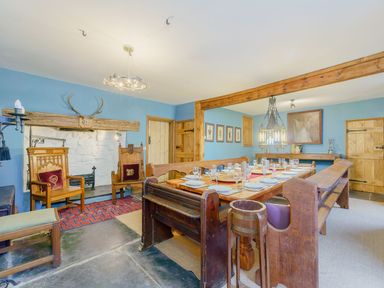 A dining room with a wooden dining table set with plates and glasses and wooden chairs at The Druids in Druid near Corwen