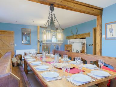 A dining room with a long wooden table set with plates and glasses and wooden benches at The Druids in Druid near Corwen