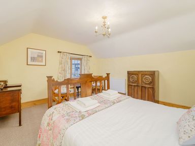 A bedroom with a wooden bed a chest of drawers a wooden cabinet a window with floral curtains and a small sitting area at The Druids in Druid near Corwen