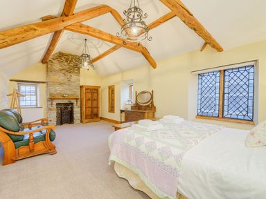A bedroom with exposed wooden beams a stone fireplace wooden furniture and leaded glass windows at The Druids in Druid near Corwen