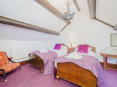 A bedroom with two single beds wooden headboards purple bedspreads and pillows a wooden chair with orange upholstery a lamp on a bedside table and exposed wooden beams on the ceiling at The Druids in Druid near Corwen
