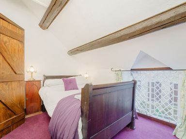 A bedroom with a wooden bed white bedding purple blanket and pillow wooden door and side table with lamps at The Druids in Druid near Corwen