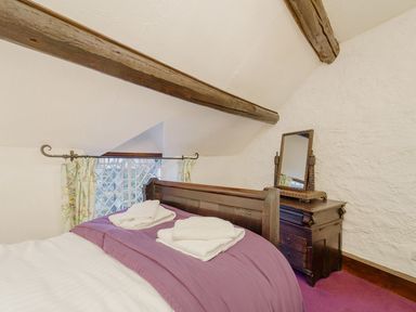 A bedroom with a wooden bed draped with purple bedding and towels on top and a wooden dresser with a mirror at The Druids in Druid near Corwen