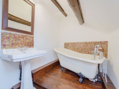 A bathroom with a pedestal sink and clawfoot bathtub on a wooden floor at The Druids in Druid near Corwen
