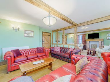 A living room with red and dark leather sofas wooden beams and a fireplace at The Druids in Druid near Corwen