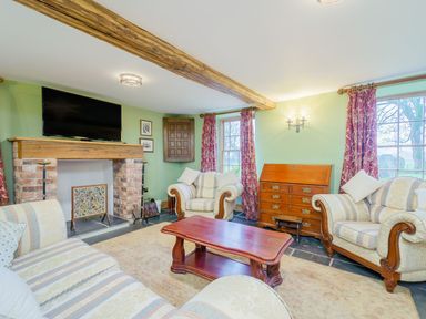 A living room with striped sofas a wooden coffee table a brick fireplace with a television above and windows with red curtains at The Druids in Druid near Corwen