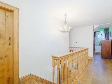 A wooden stair railing and a chandelier in a hallway with a wooden door and a chest of drawers near a window at The Druids in Druid near Corwen