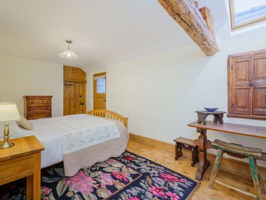 A bedroom with a wooden bed a chest of drawers a wooden desk and stools and a floral rug at The Druids in Druid near Corwen