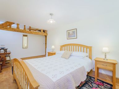 A bedroom with a wooden bed frame two bedside tables with lamps a rug and wooden beams at The Druids in Druid near Corwen