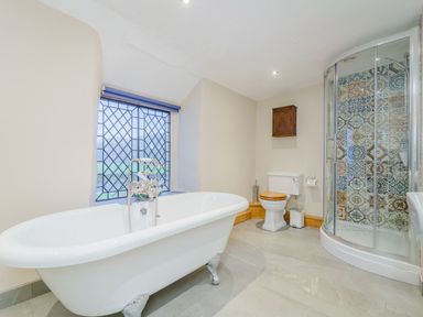 A bathroom with a clawfoot bathtub a toilet a shower with patterned tiles and a window with a grid at The Druids in Druid near Corwen