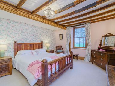 A bedroom with wooden beams on the ceiling wooden bed side tables a dresser and a window with floral curtains at The Druids in Druid near Corwen