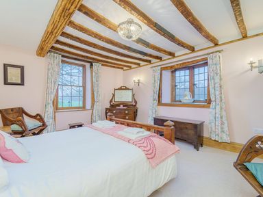 A bedroom with exposed wooden beams a double bed floral curtains wooden furniture and two windows at The Druids in Druid near Corwen