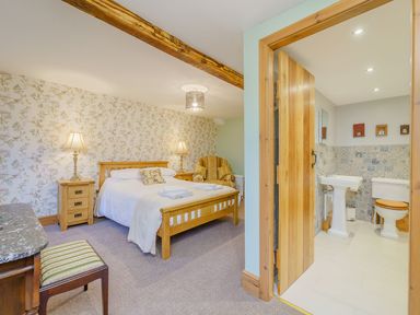 A bedroom with a wooden bed and floral wallpaper next to a bathroom with a toilet and sink at The Druids in Druid near Corwen