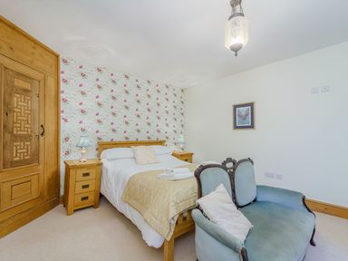 A bedroom with a double bed wooden bedside tables floral wallpaper and a blue upholstered loveseat at The Druids in Druid near Corwen
