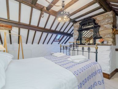 A bedroom with a metal bed frame white bedding patterned blanket wooden beams and a wall mirror at The Druids in Druid near Corwen