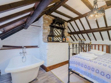 A bedroom with a metal bed, a bathtub under a slanted ceiling, wooden beams, and a decorative wall mirror at The Druids in Druid near Corwen