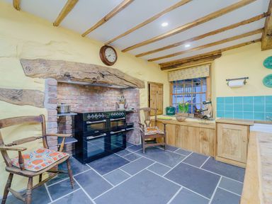 A kitchen with a brick cooking area, wooden chairs, wooden cabinets, and a window at The Druids in Druid near Corwen