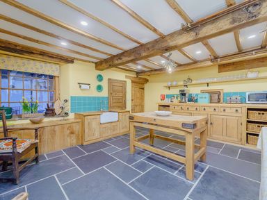 A kitchen with wooden cabinets a wooden island a stone floor and exposed ceiling beams at The Druids Druid near Corwen