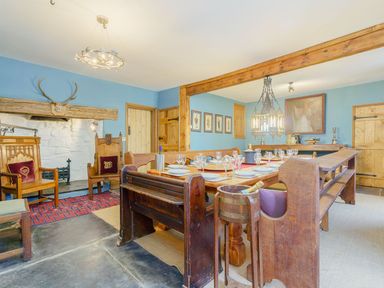 A dining room with wooden benches a large table set with plates and glasses and armchairs near a fireplace at The Druids in Druid near Corwen